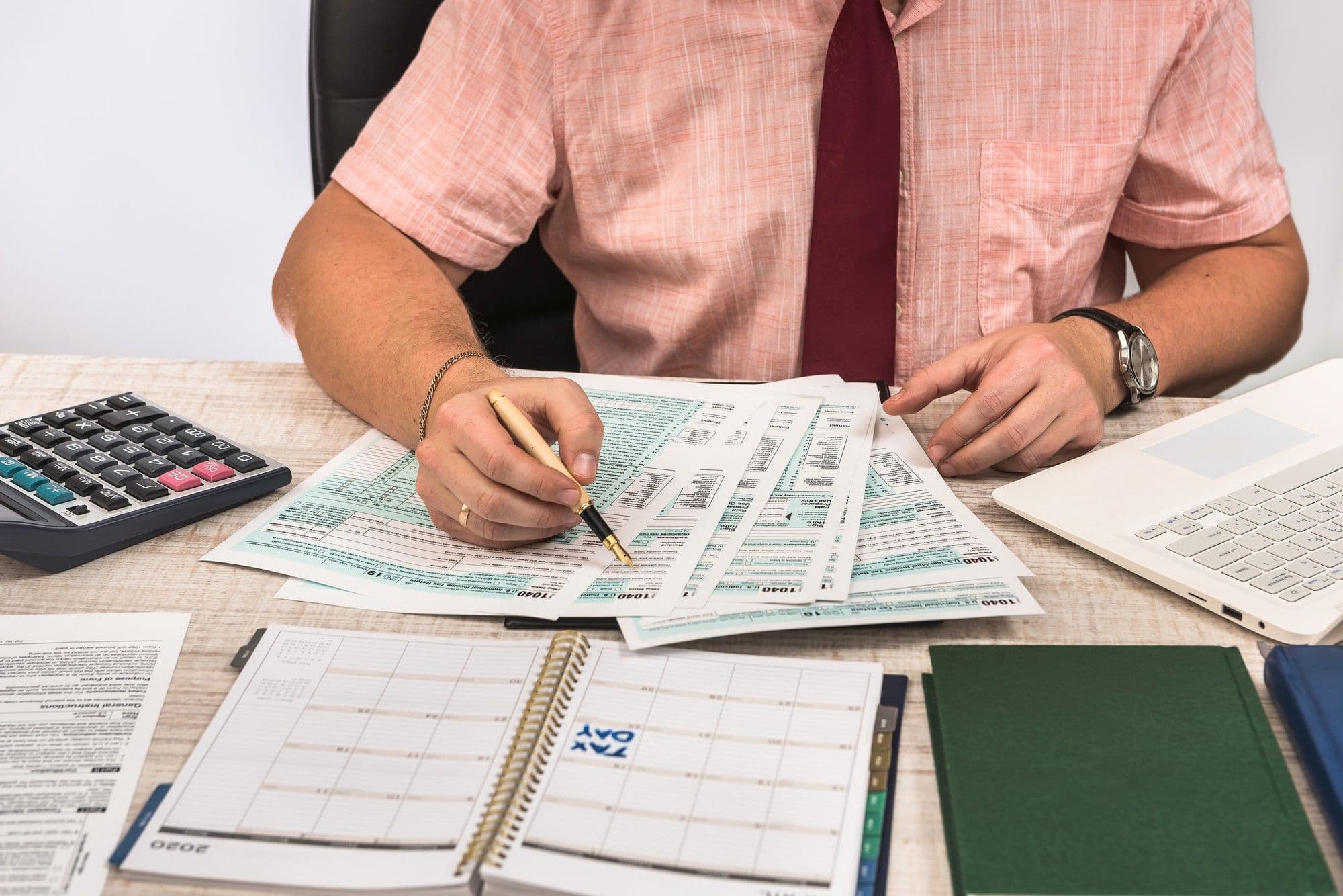 "A certified accountant reviewing tax forms at a desk, surrounded by a calculator, laptop, and planner, highlighting their vital role in financial organization and tax compliance."